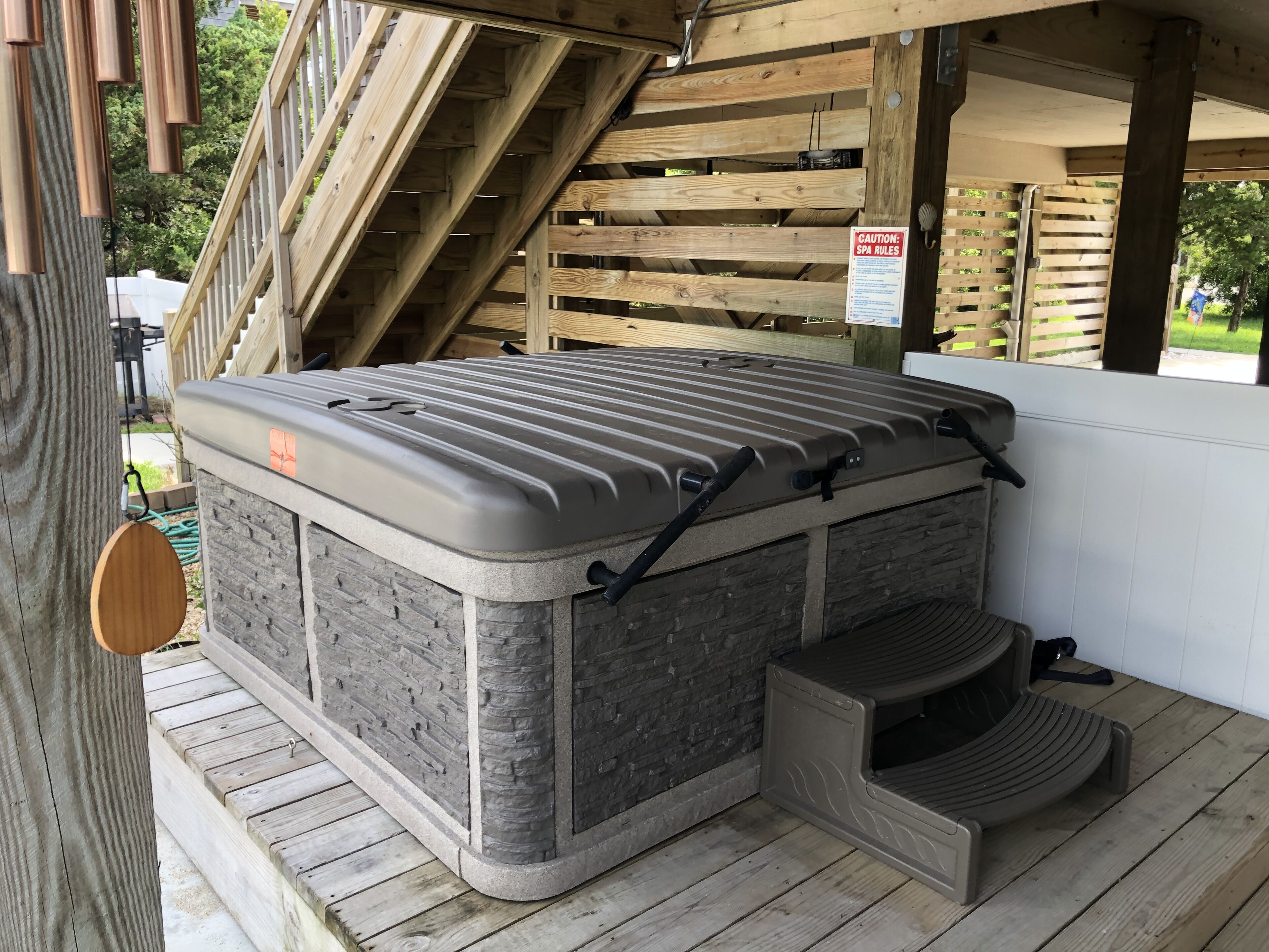 A spa hot tub with a stone exterior, a wooden deck, and a caution sign for spa rules.