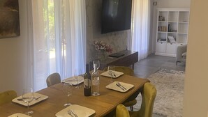 A dining area with a wooden table set for four, yellow chairs, a chandelier, a flat-screen TV mounted on the wall, and a bookshelf in the background. - Private villa with pool (Saint-Raphaël)