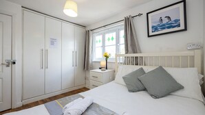 Ein Hotelzimmer mit Bett, Nachttisch, Fenster mit Vorhängen, Kleiderschrank und einem gerahmten Bild an der Wand.