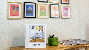 A wall of framed pictures with a welcome sign and a small table with a green pot and magazines.