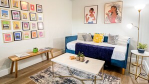 A modern bedroom with a blue sofa, a white bed, and a coffee table. There are framed pictures on the wall and a small table with a plant.