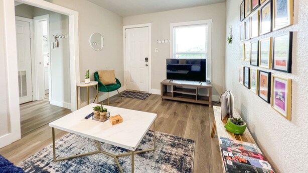 A living room with a TV, a coffee table, a chair, and a wall with framed pictures.