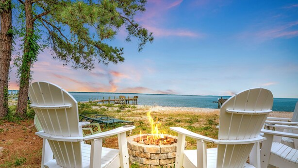 Two white Adirondack chairs facing a stone fire pit with a view of the beach and ocean. - Sea Glass Beach House!  Large sand beach, dock and hot tub! Pets welcome!  (Hague)