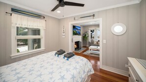 A bedroom with a bed, a ceiling fan, a fireplace, and a view of the outside. - Sea Glass Beach House!  Large sand beach, dock and hot tub! Pets welcome!  (Hague)