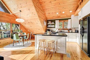 Eine moderne Küche mit Holzbalken, einer zentralen Kochinsel, Barhocker und einem Essbereich mit Stühlen.