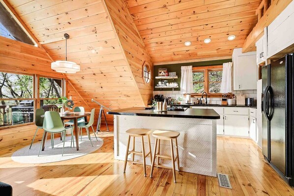 Une cuisine moderne avec des poutres en bois, un îlot central, des tabourets de bar et un coin repas avec des chaises.