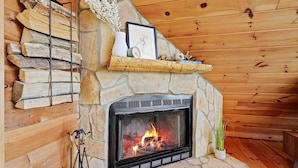 A stone fireplace with a fire, surrounded by wooden logs and a shelf with decorative items. - Modern Mountaintop A-Frame | Wineries, Views, Lake (Morganton)