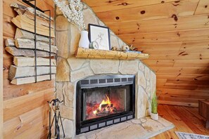 Ein Steinkamin mit Feuer, umgeben von Holzscheiten und einem Regal mit Dekorationen.