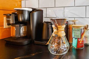 Eine Kaffeemaschine, eine Glas-Kaffeekanne sowie Gläser mit Honig und Gewürzen auf einer Küchenarbeitsplatte.