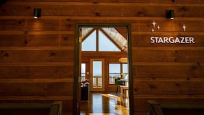 A wooden cabin interior with a sign reading "STARGAZER," a dining area with chairs and a table, and a view through the door. - Modern Mountaintop A-Frame | Wineries, Views, Lake (Morganton)