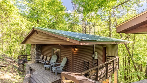 Une cabane dotée d’une terrasse, de deux fauteuils Adirondack et d’un mur en pierre.