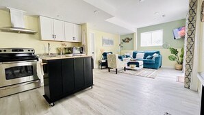 Eine moderne Küche mit Herd, Schränken und einer schwarzen Kochinsel. Es gibt einen Wohnbereich mit einem blauen Sofa und einem Fernseher.