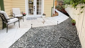 Eine Terrasse mit zwei Stühlen, einer Tür und einem kleinen Garten.