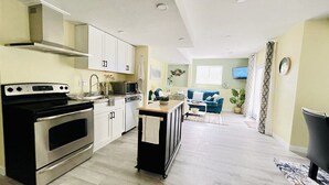 Eine moderne Küche mit Edelstahlgeräten, ein Essbereich mit einem blauen Sofa und ein Wohnzimmer mit Fernseher.