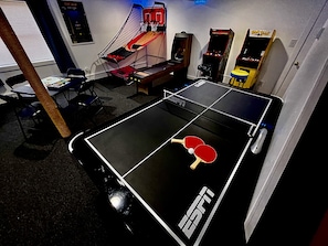 Una mesa de ping pong con dos paletas, un aro pequeño de baloncesto y una máquina arcade Pac-Man.