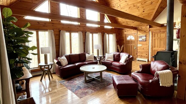 A spacious living room with wooden floors, a ceiling fan, leather sofas, and a fireplace. - Pocono Chalet Cabin Sauna Game Room Fire Pit Pools (Bushkill)