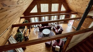 A wooden cabin interior with a loft bedroom, a living area with leather sofas, and a dining table. - Pocono Chalet Cabin Sauna Game Room Fire Pit Pools (Bushkill)