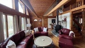 A cozy cabin interior with wooden walls, a fireplace, leather sofas, and a staircase leading to an upper level. - Pocono Chalet Cabin Sauna Game Room Fire Pit Pools (Bushkill)