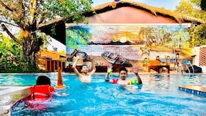 A swimming pool with a mural on the wall, a thatched roof structure, and a tree in the background.