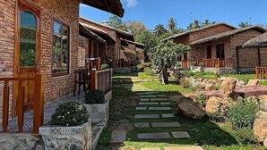A row of rustic brick houses with thatched roofs, a paved pathway, and a small garden area.