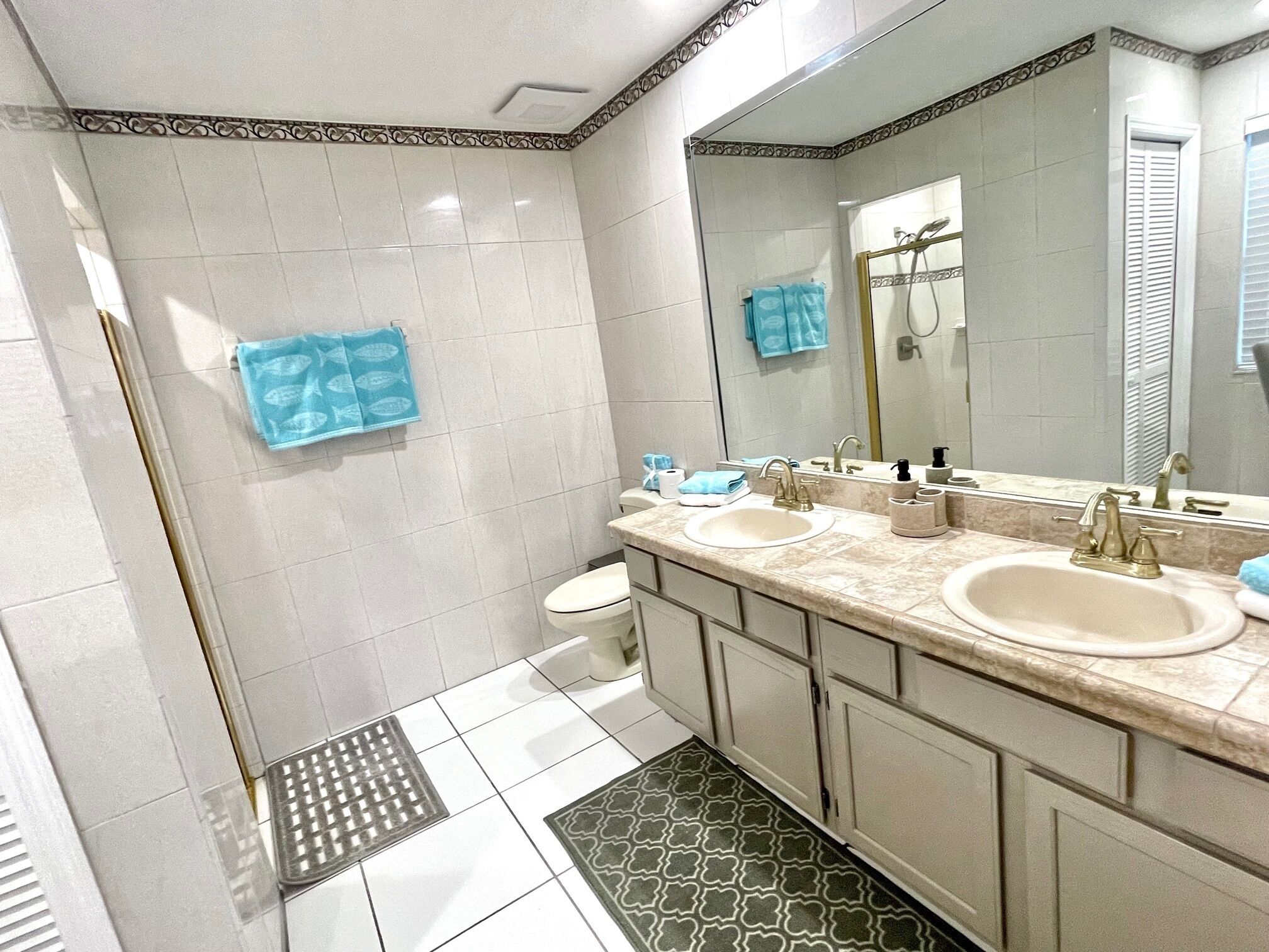 Une salle de bain avec deux lavabos, des toilettes, une douche et un grand miroir.