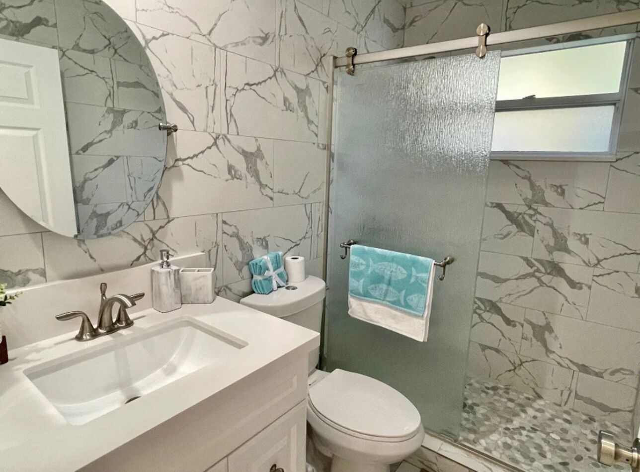 A bathroom with a marble backsplash, a white sink, a toilet, and a shower curtain.