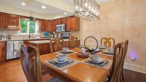 Una cocina moderna con armarios de madera, una isla central y un comedor con una mesa de madera preparada para seis comensales.