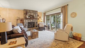 Una sala de estar acogedora con chimenea de piedra, sofá de cuero y un amplio ventanal con cortinas.