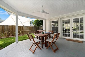 A covered patio with a wooden table and chairs, a ceiling fan, and a view of the backyard.
