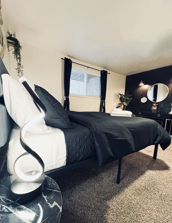 A modern bedroom with a black bed, a round mirror, and a small round table with a lamp. - Ebony Escape- gym, sauna, hot tub, seasonal pool (Corvallis)