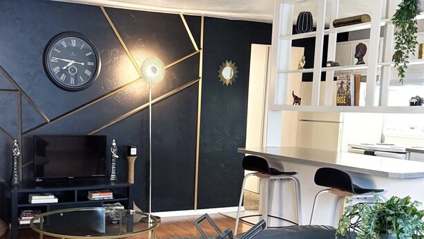 Un salon moderne avec un canapé d’angle noir, une table basse en verre et une bibliothèque blanche.