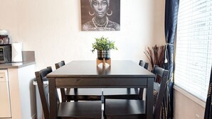 Un coin repas avec une table et des chaises en bois, un ventilateur de plafond, un tableau accroché au mur et une fenêtre avec des rideaux.