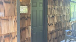 Fachada de madera con una puerta verde, un felpudo y un banco.
