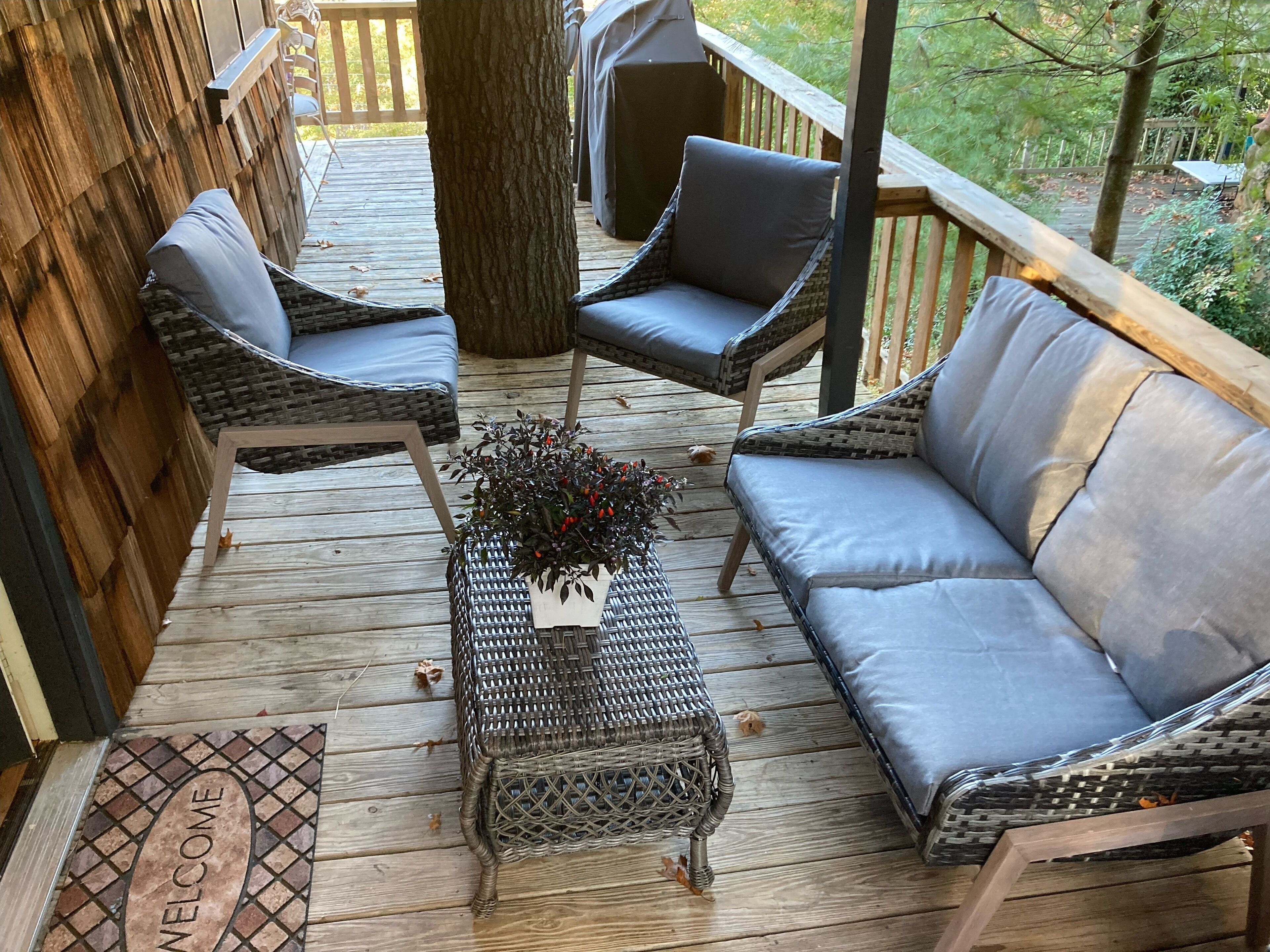 A wooden deck with wicker furniture, including two chairs and a sofa, and a welcome mat.