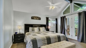 Une chambre à coucher avec un grand lit, une table de chevet, une lampe, un ventilateur de plafond et une fenêtre avec des rideaux.