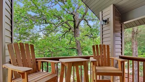 Une terrasse en bois, agrémentée de chaises Adirondack et d’une table, qui offre une vue sur un paysage verdoyant et luxuriant, parsemé d’arbres.