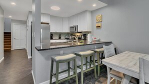 Une cuisine moderne avec des meubles blancs, un grand îlot central doté de tabourets, et un coin repas avec une table et des chaises.