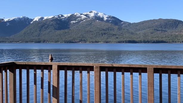 Une jetée en bois offrant une vue sur un lac paisible et, au loin, sur des montagnes enneigées.