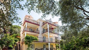 Ein mehrstöckiges Hotel mit Balkonen, einer überdachten Außenbereich-Sitzgelegenheit und einem Garten.