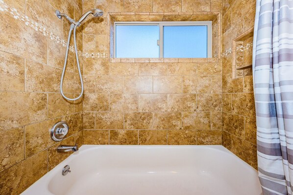 A bathroom with a bathtub, a shower, and a window.