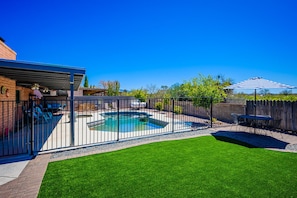 A backyard with a swimming pool, a fenced patio area, and a lawn.