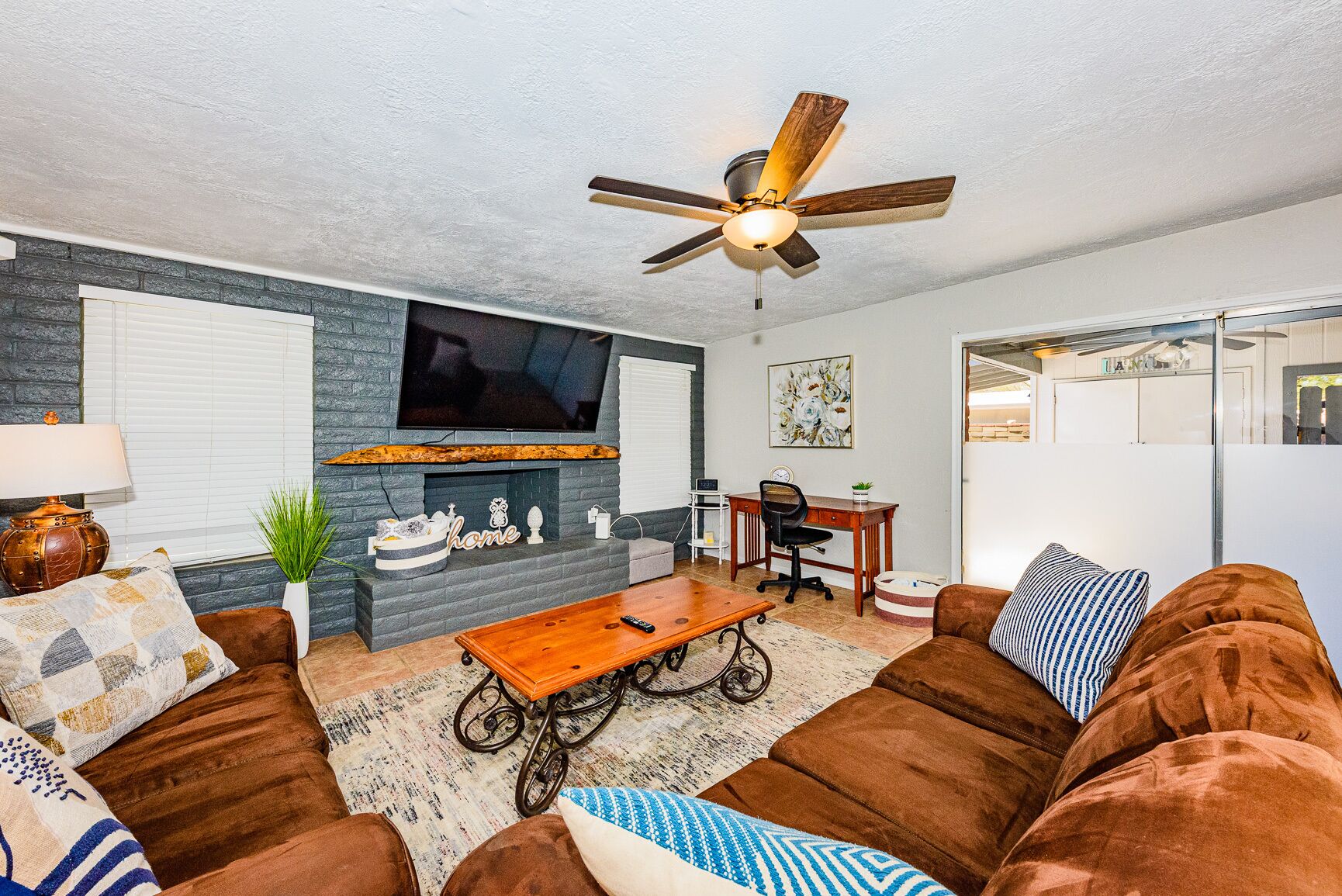 A living room with a fireplace, a television, a ceiling fan, and a desk with a chair.