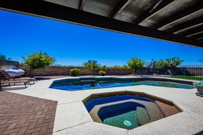 A swimming pool with a hot tub, lounge chairs, and a brick patio.