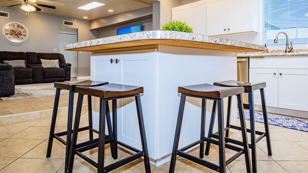 A modern kitchen with a marble countertop, two stools, white cabinets, and a ceiling fan. - Casa De Azul ~ Fabulous Private Pool Paradise ~ Spacious And Comfy! (Tucson)