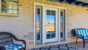 A covered patio with two wicker chairs, a patterned rug, and a sliding glass door leading to a pool. - Casa De Azul ~ Fabulous Private Pool Paradise ~ Spacious And Comfy! (Tucson)