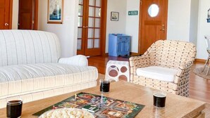 A living room with a sofa, a wicker chair, a coffee table with a board game, and a bowl of popcorn.
