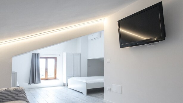 Ein modernes Schlafzimmer mit Bett, einem an der Wand montierten Fernseher und einem Fenster mit Vorhängen.