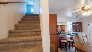 Un escalier menant à un espace cuisine équipé d’une table à manger et de tabourets de bar.