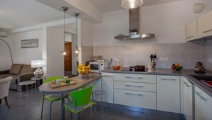A modern kitchen with white cabinets, a central island with chairs, a hanging light fixture, and a microwave. - Casa Chjara Maria (Vescovato)
