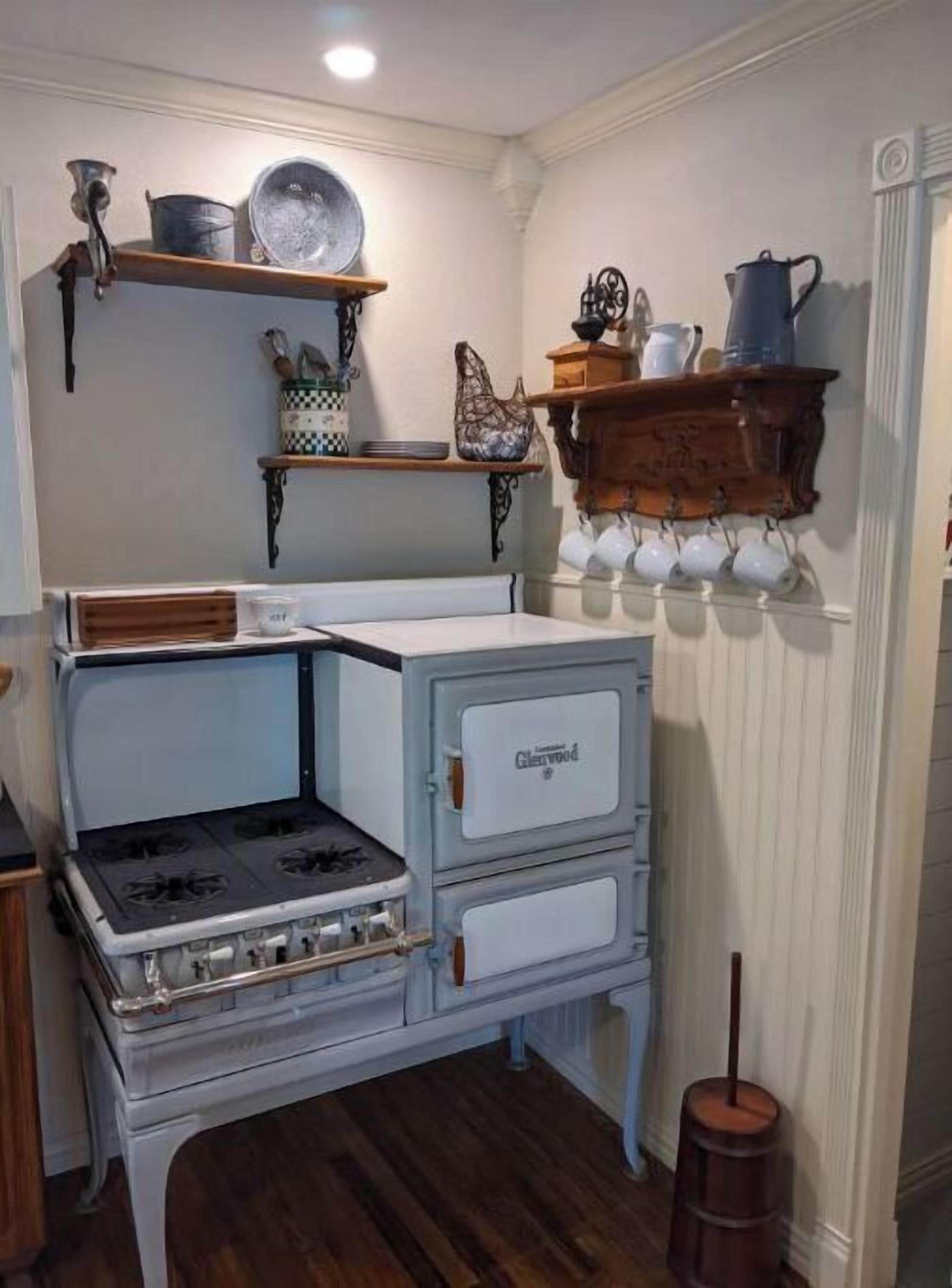 A kitchen with a vintage stove, wooden shelves, and a hanging pot rack.